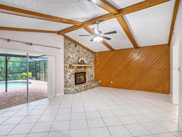 unfurnished living room with wooden walls, vaulted ceiling with beams, ceiling fan, a fireplace, and a textured ceiling