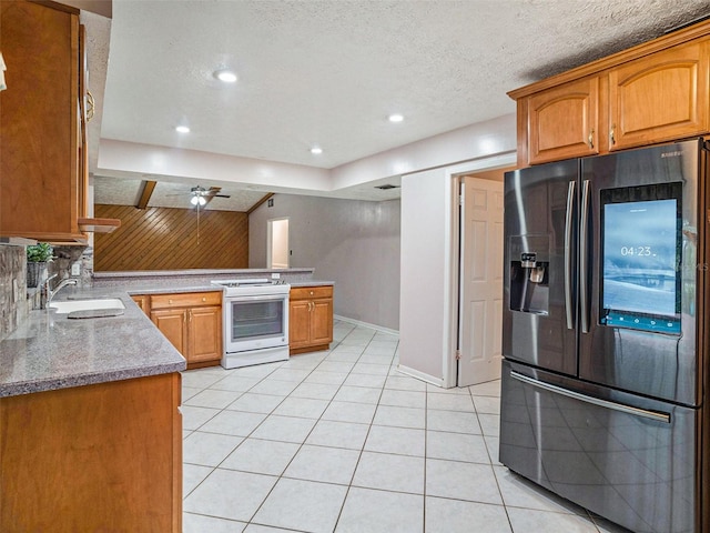 kitchen with a peninsula, electric range, light tile patterned flooring, stainless steel fridge with ice dispenser, and a sink