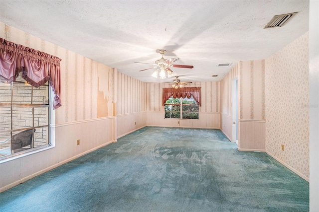 empty room with visible vents, a textured ceiling, and wallpapered walls