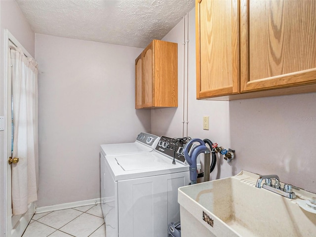 laundry area featuring light tile patterned flooring, cabinet space, a sink, a textured ceiling, and washer and dryer