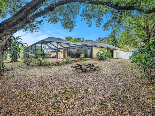 back of property featuring a gate, stucco siding, glass enclosure, and fence