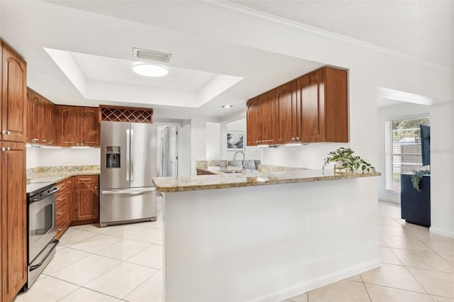 kitchen with a tray ceiling, light tile patterned floors, a peninsula, stainless steel appliances, and a sink