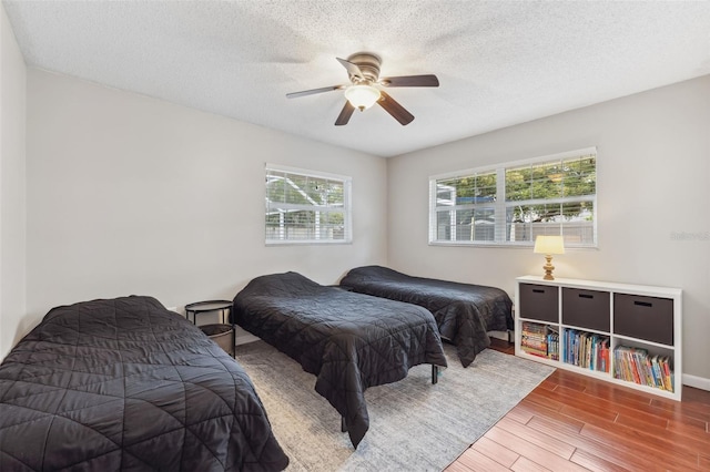 bedroom with baseboards, a textured ceiling, a ceiling fan, and wood finished floors