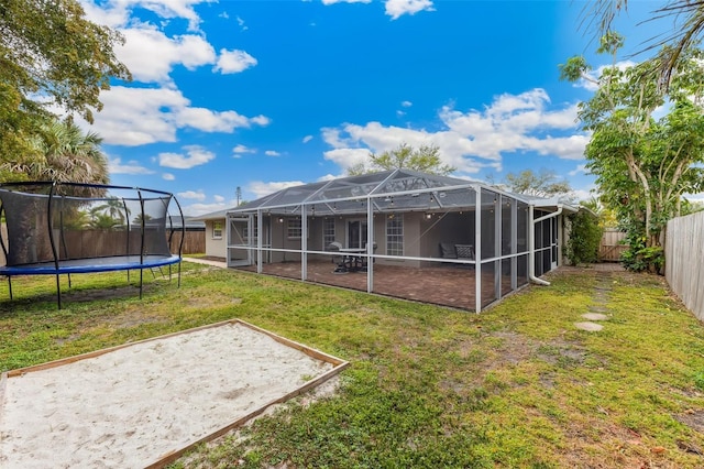 rear view of house with a fenced backyard, a yard, a lanai, and a trampoline