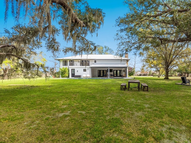 back of house with a balcony, a chimney, and a yard