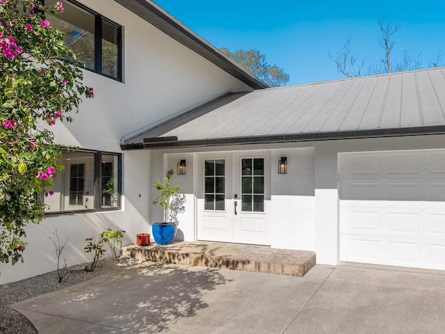 view of exterior entry with metal roof, an attached garage, french doors, stucco siding, and a standing seam roof