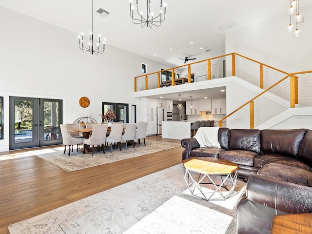 living area with hardwood / wood-style flooring, visible vents, a towering ceiling, french doors, and an inviting chandelier