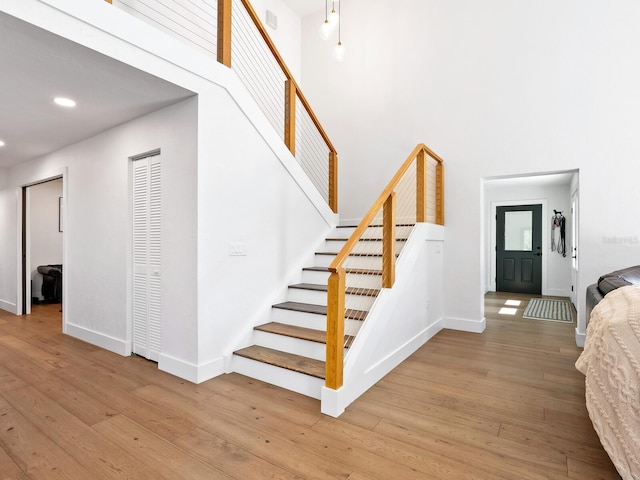 stairs with recessed lighting, wood finished floors, a towering ceiling, and baseboards