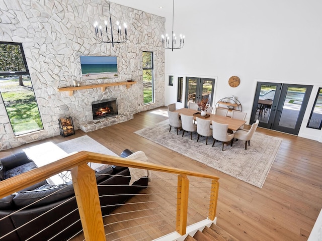 living room with hardwood / wood-style flooring, a fireplace, a towering ceiling, french doors, and an inviting chandelier