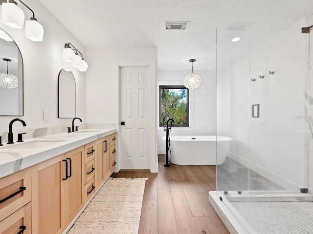 bathroom featuring double vanity, visible vents, hardwood / wood-style flooring, a shower stall, and a sink