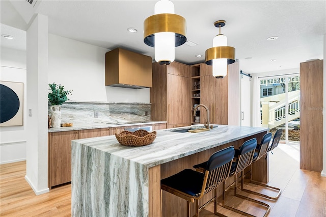 kitchen with light stone counters, hanging light fixtures, a barn door, a sink, and modern cabinets