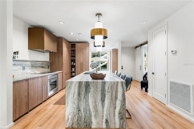 kitchen with a barn door, stainless steel oven, visible vents, and light wood-style floors