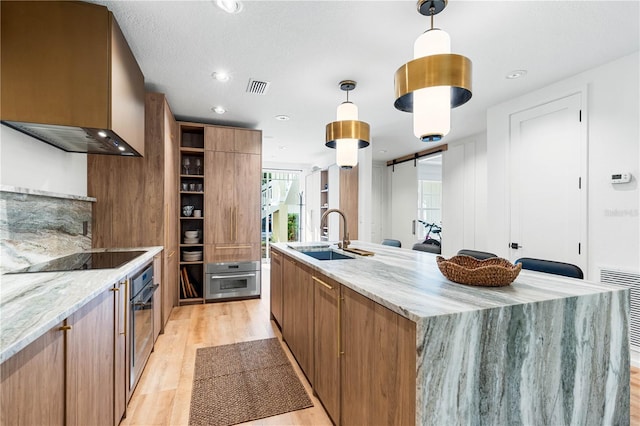 kitchen with black electric stovetop, a barn door, a sink, stainless steel oven, and open shelves