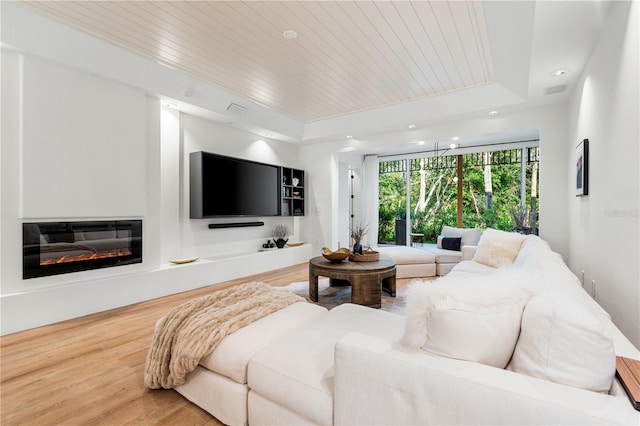 living area with visible vents, a raised ceiling, a glass covered fireplace, wood ceiling, and wood finished floors