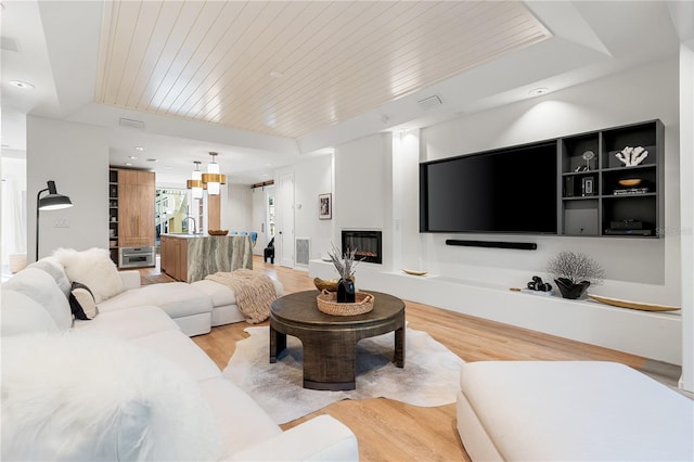 living room featuring light wood-style floors, a glass covered fireplace, wooden ceiling, and visible vents