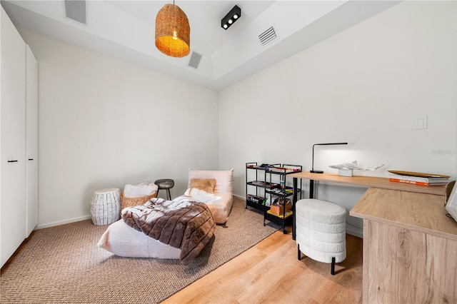 bedroom with a tray ceiling, baseboards, visible vents, and wood finished floors