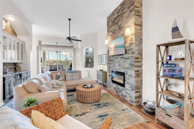 living room featuring light wood-style floors, ceiling fan, and a stone fireplace