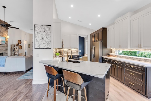 kitchen with a breakfast bar area, a fireplace, a sink, stainless steel fridge with ice dispenser, and light stone countertops