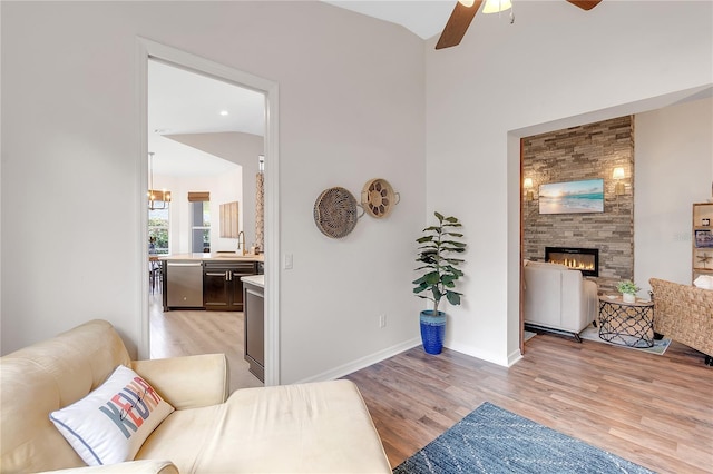 living room with lofted ceiling, ceiling fan, a fireplace, baseboards, and light wood-type flooring