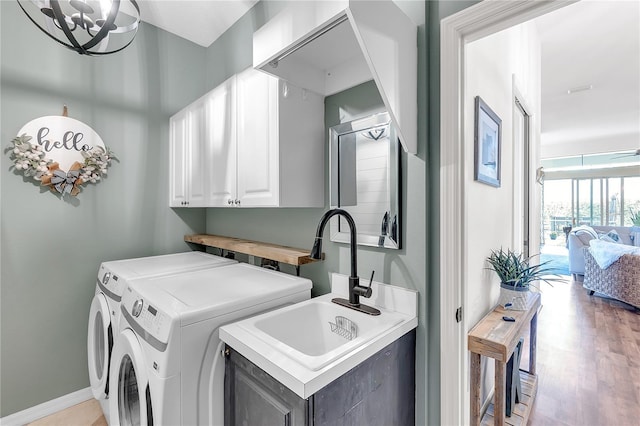 washroom featuring cabinet space, light wood-style floors, washing machine and dryer, a sink, and baseboards