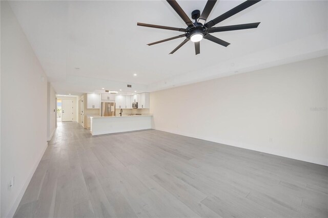 unfurnished living room featuring a ceiling fan, light wood-style floors, and baseboards