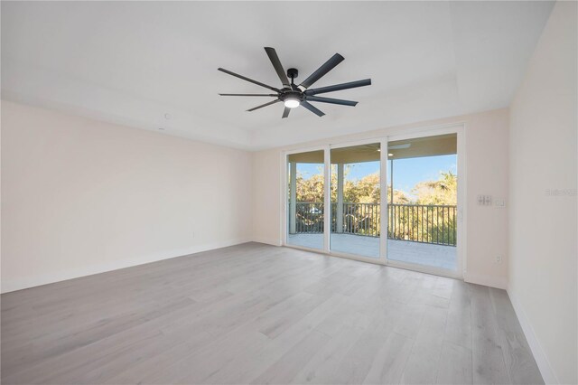 spare room with a raised ceiling, light wood-style floors, baseboards, and ceiling fan