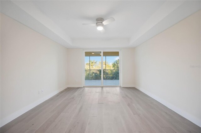 spare room featuring light wood-style flooring, baseboards, a tray ceiling, and a ceiling fan