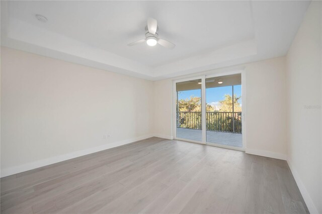 empty room featuring ceiling fan, baseboards, a tray ceiling, and wood finished floors