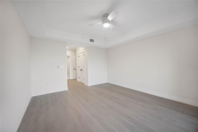 empty room with a tray ceiling, visible vents, baseboards, and wood finished floors