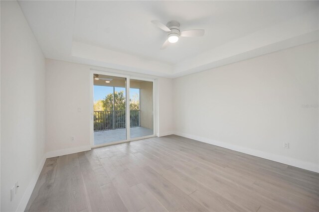 empty room with a raised ceiling, light wood-style flooring, a ceiling fan, and baseboards