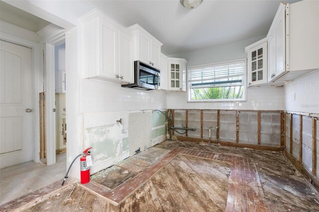 kitchen featuring tasteful backsplash, stainless steel microwave, white cabinets, and glass insert cabinets