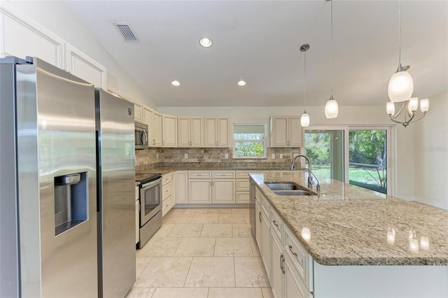 kitchen with a sink, visible vents, appliances with stainless steel finishes, decorative backsplash, and an island with sink