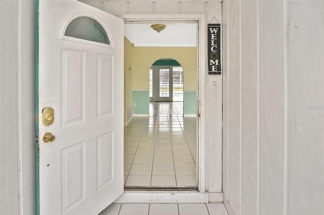 corridor with arched walkways, crown molding, and tile patterned floors