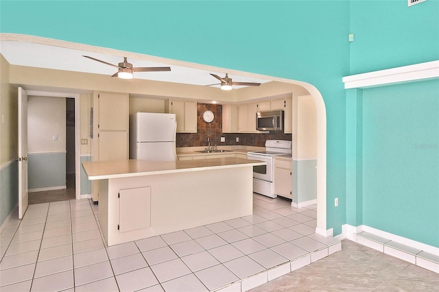 kitchen featuring arched walkways, light countertops, a kitchen island, a sink, and white appliances