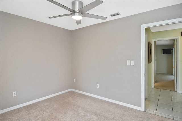 spare room featuring baseboards, visible vents, a ceiling fan, light colored carpet, and light tile patterned flooring