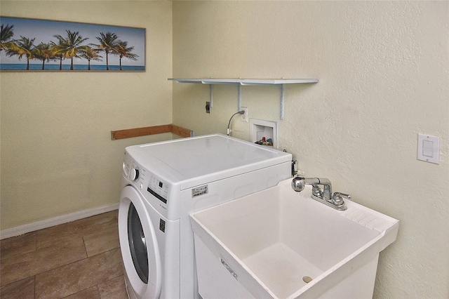 clothes washing area featuring a textured wall, laundry area, a sink, baseboards, and washer / clothes dryer