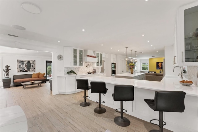 kitchen with white cabinets, light wood-style flooring, custom range hood, light countertops, and backsplash