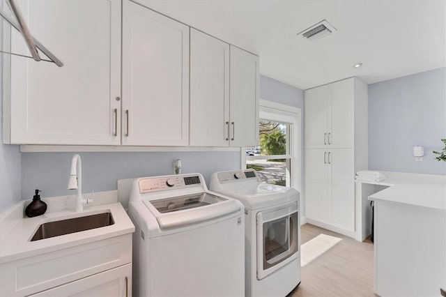 laundry area with washing machine and clothes dryer, cabinet space, visible vents, light wood-style floors, and a sink