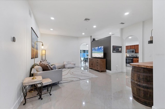 living room with arched walkways, visible vents, baseboards, and recessed lighting