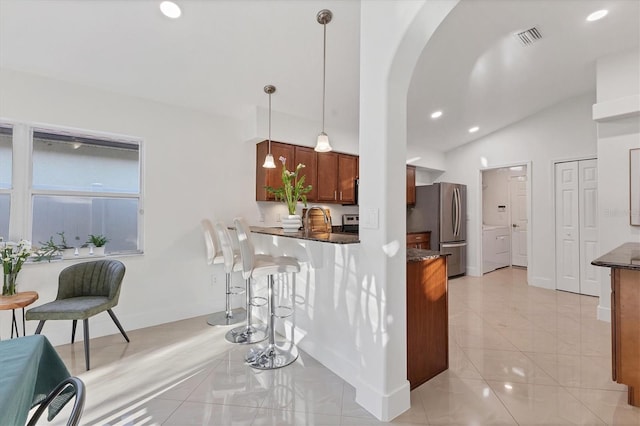 kitchen with visible vents, arched walkways, brown cabinetry, dark stone countertops, and freestanding refrigerator