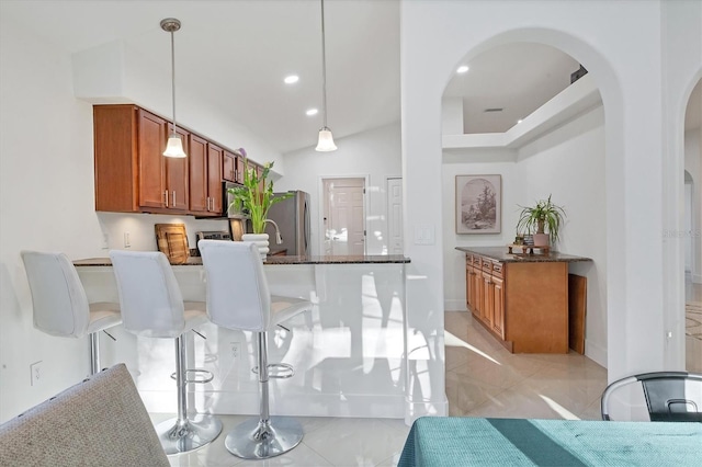 kitchen featuring arched walkways, brown cabinetry, dark stone counters, and freestanding refrigerator