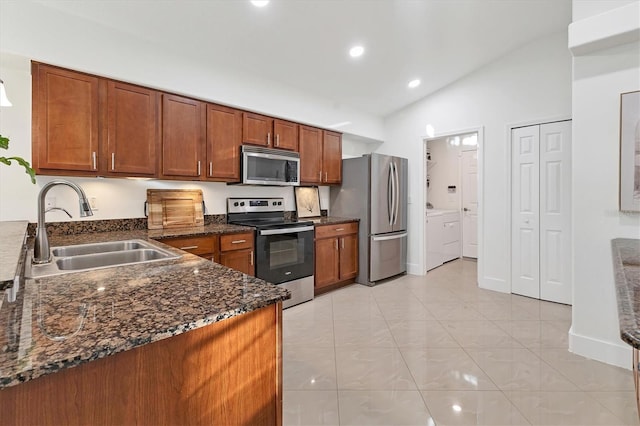 kitchen featuring stainless steel appliances, lofted ceiling, brown cabinetry, washing machine and dryer, and a sink