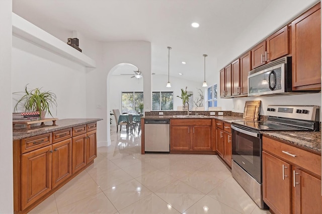 kitchen featuring arched walkways, stainless steel appliances, a sink, and brown cabinets