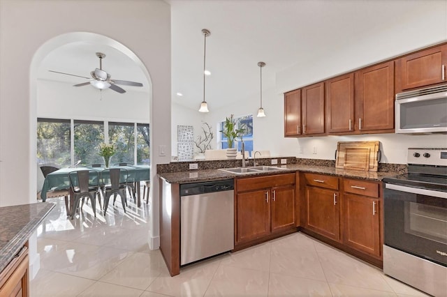 kitchen with brown cabinets, dark stone counters, stainless steel appliances, and a sink