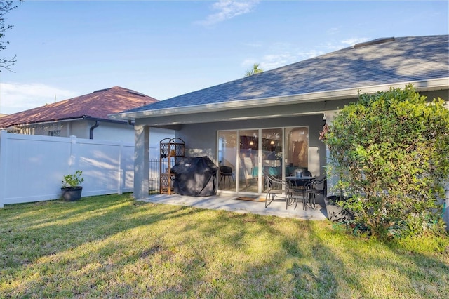 rear view of property featuring a patio, fence, a yard, roof with shingles, and stucco siding