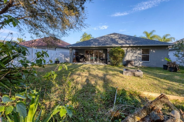 back of house featuring a shingled roof, stucco siding, a lawn, and fence