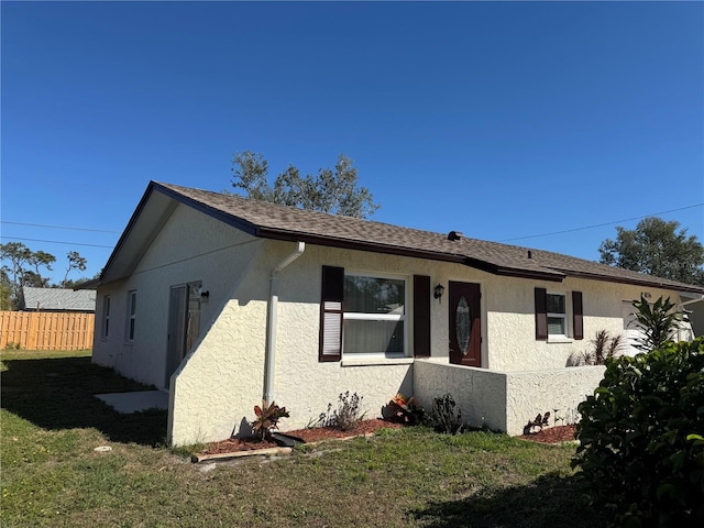 view of front facade featuring a front yard, roof with shingles, fence, and stucco siding