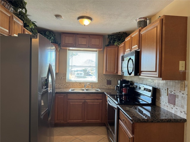 kitchen featuring light tile patterned floors, stainless steel appliances, a sink, and brown cabinetry