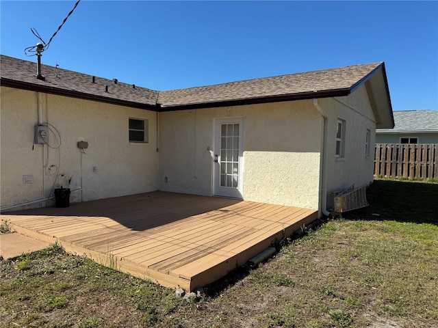 rear view of property featuring a deck, a shingled roof, fence, and stucco siding