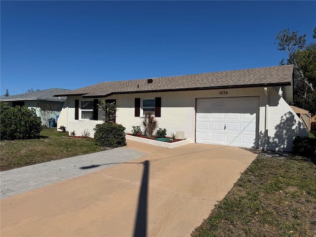 ranch-style home featuring a garage, a shingled roof, driveway, stucco siding, and a front yard